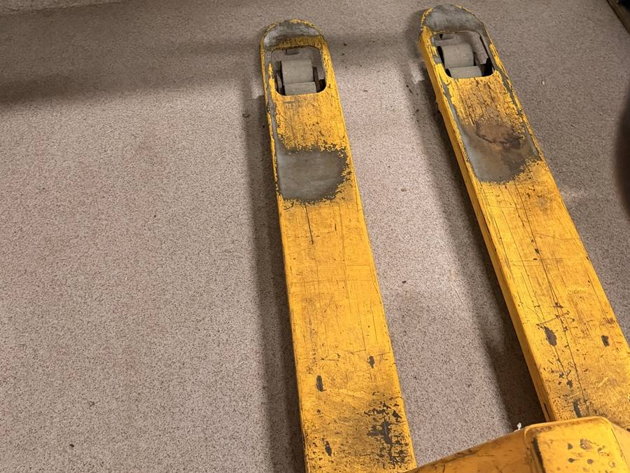 Gabeln eines gelben Handhubwagens auf dem Hallenboden
